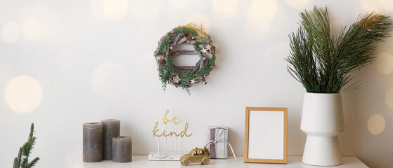 Christmas wreath hanging on white wall near table with stylish decorations in room