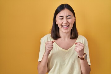 Hispanic girl wearing casual t shirt over yellow background excited for success with arms raised and eyes closed celebrating victory smiling. winner concept.