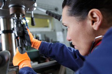 Fototapeta na wymiar metal worker woman operating drilling machine concentrating on her job