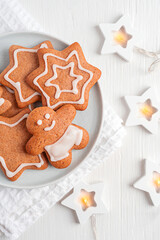 Top view of homemade baked organic gingerbread cookies or crunchy biscuits made with ginger spice and cinnamon decorated with sugar icing served on plate on white wooden table with glowing garland