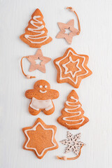 Flat lay of homemade baked organic gingerbread cookies or crunchy biscuits made with ginger spice and cinnamon decorated with sugar icing served on white wooden background with christmas decorations