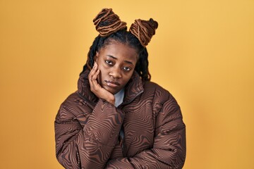 African woman with braided hair standing over yellow background thinking looking tired and bored with depression problems with crossed arms.