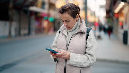 Middle age hispanic woman using smartphone at street