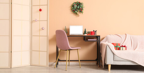 Modern workplace with laptop, Christmas gifts, wreath and sofa in light room