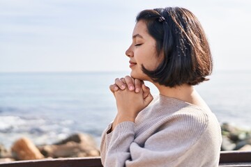 Young woman smiling confident praying at seaside - obrazy, fototapety, plakaty