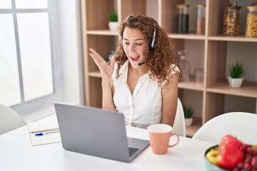 Young caucasian woman wearing call center agent headset working from home screaming proud, celebrating victory and success very excited with raised arm