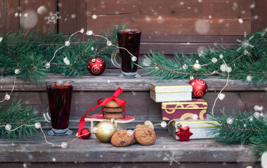 Glasses of mulled wine, gift boxes, chocolate chip cookies, pine branches and glowing christmas lights on steps of rustic wooden ladder. Christmas concept.
