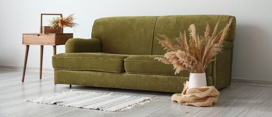 Interior of modern room with green sofa and table with reeds in vase