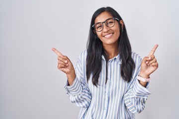 Young hispanic woman wearing glasses smiling confident pointing with fingers to different directions. copy space for advertisement