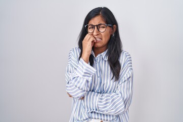 Young hispanic woman wearing glasses looking stressed and nervous with hands on mouth biting nails. anxiety problem.