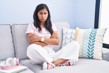 Young hispanic woman sitting on the sofa at home skeptic and nervous, disapproving expression on face with crossed arms. negative person.