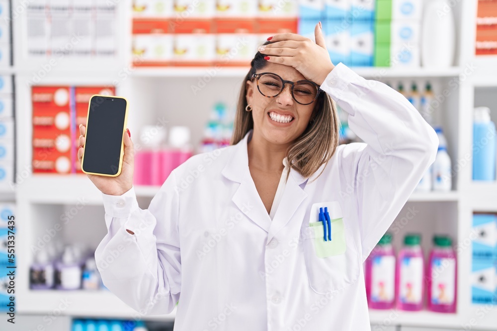 Sticker Blonde woman working at pharmacy drugstore showing smartphone screen stressed and frustrated with hand on head, surprised and angry face