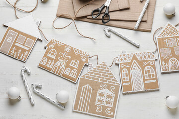Cardboard houses with Christmas balls and candy canes on white wooden background