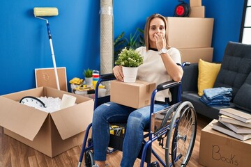 Young woman sitting on wheelchair moving to a new home laughing and embarrassed giggle covering...