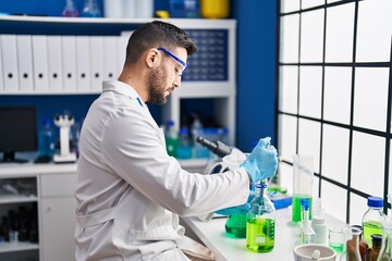 Young hispanic man wearing scientist uniform measuring liquid at laboratory