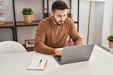 Young hispanic man using laptop sitting on table at home