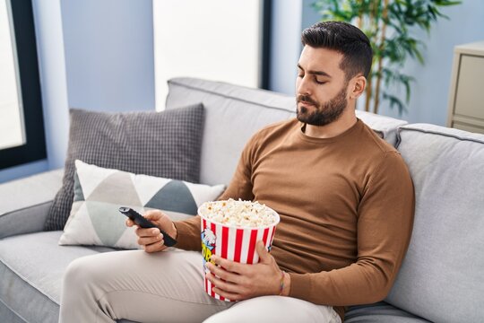 Young Hispanic Man Boring Watching Movie Sitting On Sofa At Home