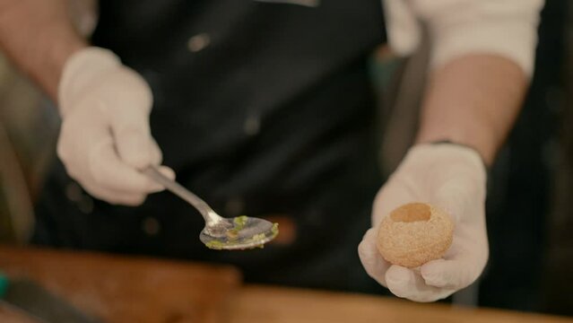 the waiter punches a hole in the panipuri with a spoon to stuff it.