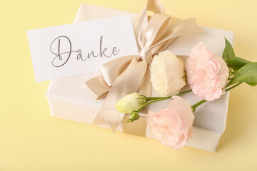 Gift box, card with text DANKE and eustoma flowers on color background, closeup