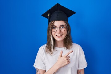 Blonde caucasian woman wearing graduation cap cheerful with a smile of face pointing with hand and...