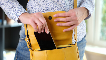 Woman in casual clothes put her smartphone in bright yellow shoulder bag.