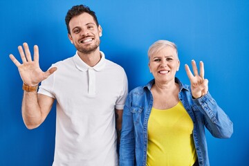 Young brazilian mother and son standing over blue background showing and pointing up with fingers number eight while smiling confident and happy.
