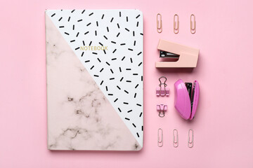 Composition with notebook, staplers and paper clips on pink background