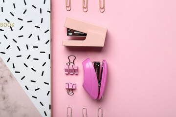Composition with notebook, staplers and paper clips on pink background, closeup
