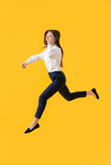 Fototapeta na wymiar Young assistant talking by mobile phone and jumping on yellow background