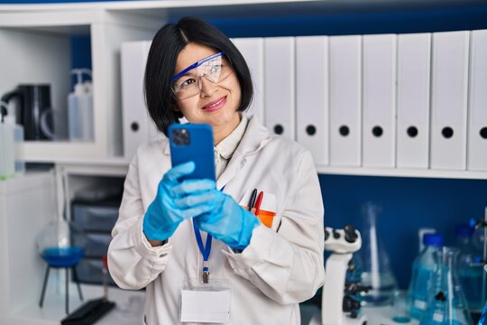 Young chinese woman scientist using smartphone working at laboratory