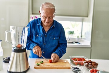 Senior man smiling confident cutting strawberry at kitchen