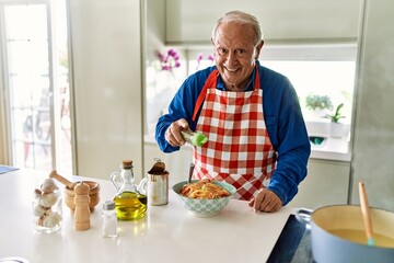 Senior man smiling confident pouring oregano on spaghetti at kitchen