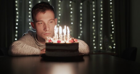 Sad young man looking at birthday cake with candles alone