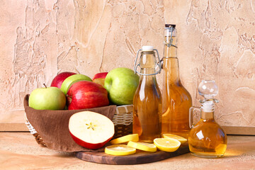 Bottles of apple cider vinegar and basket with fresh fruits on color table