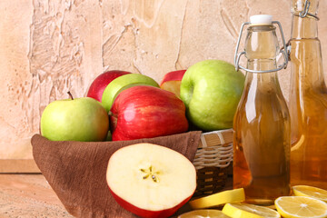 Bottles of apple cider vinegar and fresh fruits on color table, closeup