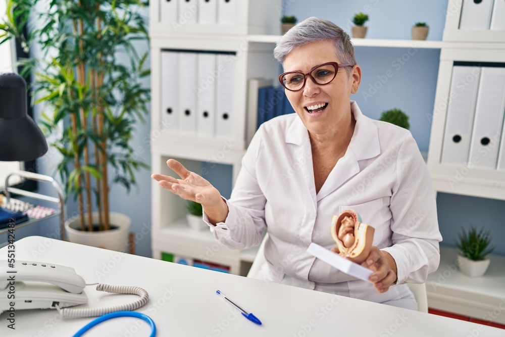 Poster Middle age woman wearing gynecologist uniform holding uterus with fetus at clinic