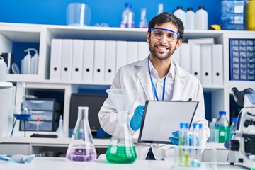 Young hispanic man scientist smiling confident write on clipboard at laboratory