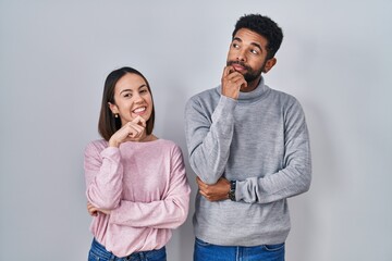 Naklejka premium Young hispanic couple standing together with hand on chin thinking about question, pensive expression. smiling and thoughtful face. doubt concept.