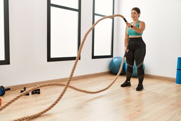Young beautiful hispanic woman smiling confident using battle rope training at sport center