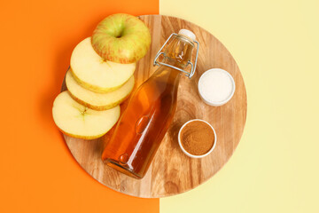Wooden board with cut apple, bottle of juice, sugar and cinnamon powder on color background