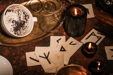 Cup with spent coffee grounds and runes for fortune telling on table