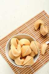 Bamboo mat with bowl of fortune cookies on light background, closeup