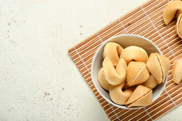 Bamboo mat with bowl of fortune cookies on light background, closeup