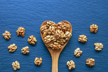 Fototapeta na wymiar Halves of walnut kernels in heart-shaped spoon. Copy space