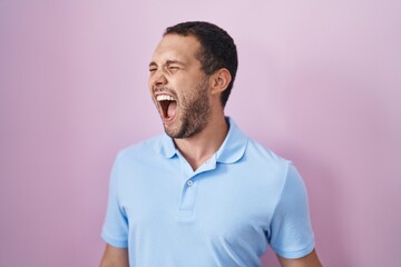 Fototapeta premium Hispanic man standing over pink background angry and mad screaming frustrated and furious, shouting with anger. rage and aggressive concept.