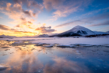 North, Norway. Winter landscape during sunset. Bright sky. Ice and snow on the shore. Reflections on the ice surface. Snowy winter. Natural northern landscape on the Lofoten Islands.