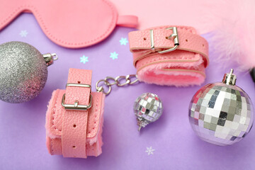 Handcuffs from sex shop and Christmas balls on lilac background, closeup