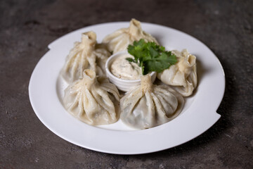 khinkali on a white plate with sauce and herbs on a gray background