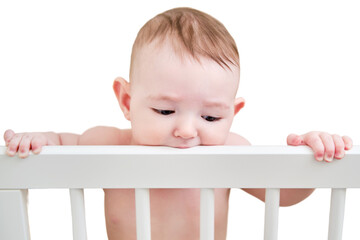 Baby gnaws at the edge crib during teething itching, isolated on a white background. Funny child...