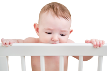 Baby gnaws at the edge crib during teething itching, isolated on a white background. Funny child scratching his teeth on the rail bed, age six months